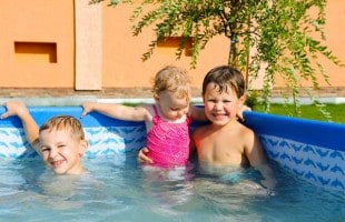 Two young boys pose with their baby sister in an above ground pool